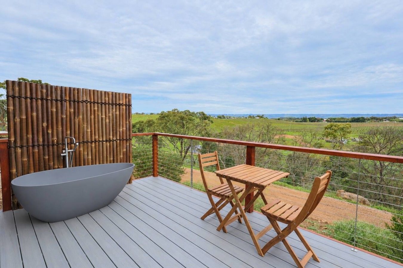A deck with a large bathtub, wooden chairs, and a table.