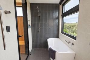 A modern bathroom with a freestanding bathtub, a showerhead, and a window offering a view of the outdoors. - Westringia retreat with sauna and outdoor bath (McLaren Vale)