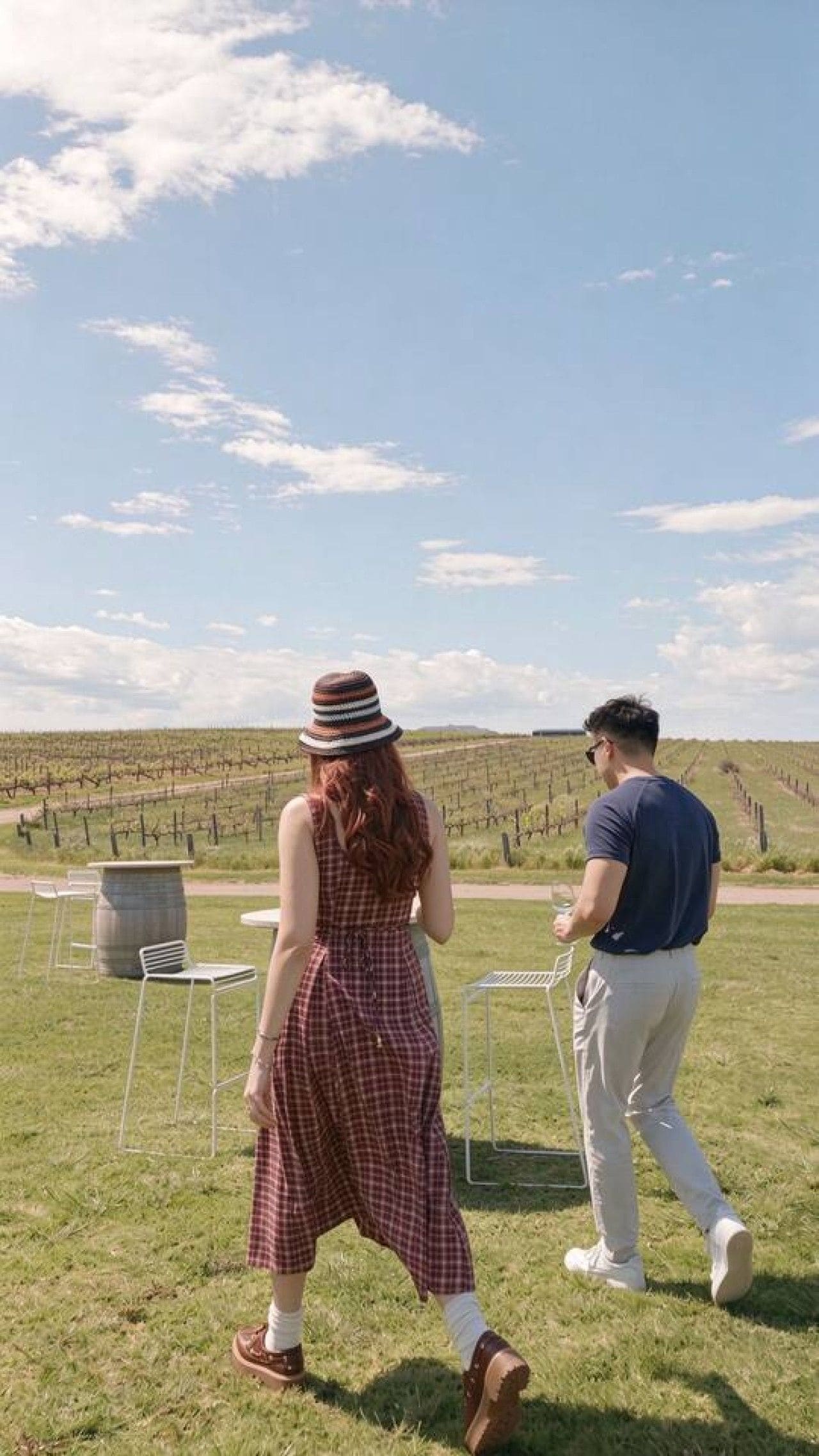 Two people walking in a vineyard with rows of grapevines and a clear sky.