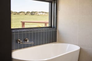 Een moderne badkamer met een vrijstaand bad, een raam met uitzicht op een grasveld en een betegelde muur.