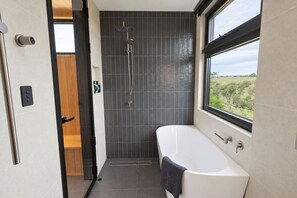 A modern bathroom with a bathtub, shower, and a view through a window. - Grevillea vineyard cabin with outdoor bath (McLaren Vale)
