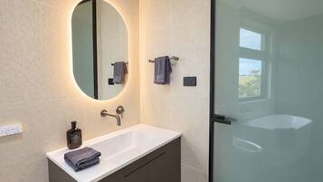 A modern bathroom with a white sink, a large mirror, and a glass shower enclosure.