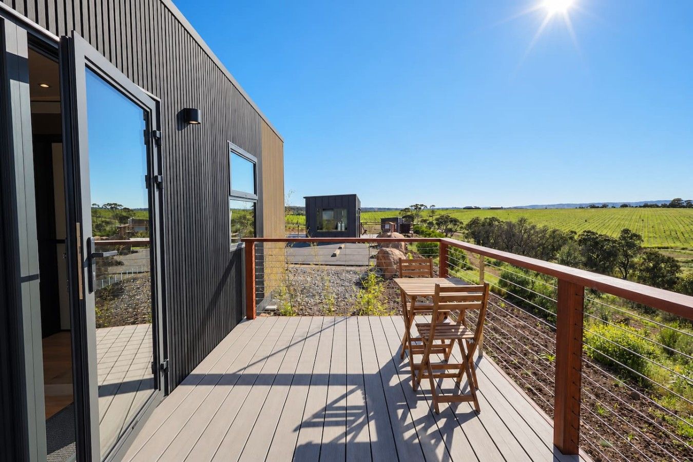 An outdoor deck with a wooden table and chairs, a TV, and a view of a green field.