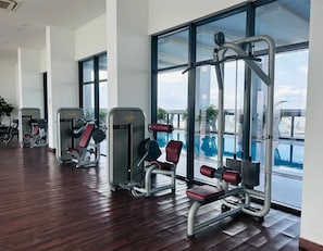 Et fitnesscenter med diverse træningsmaskiner, store vinduer og trægulv.