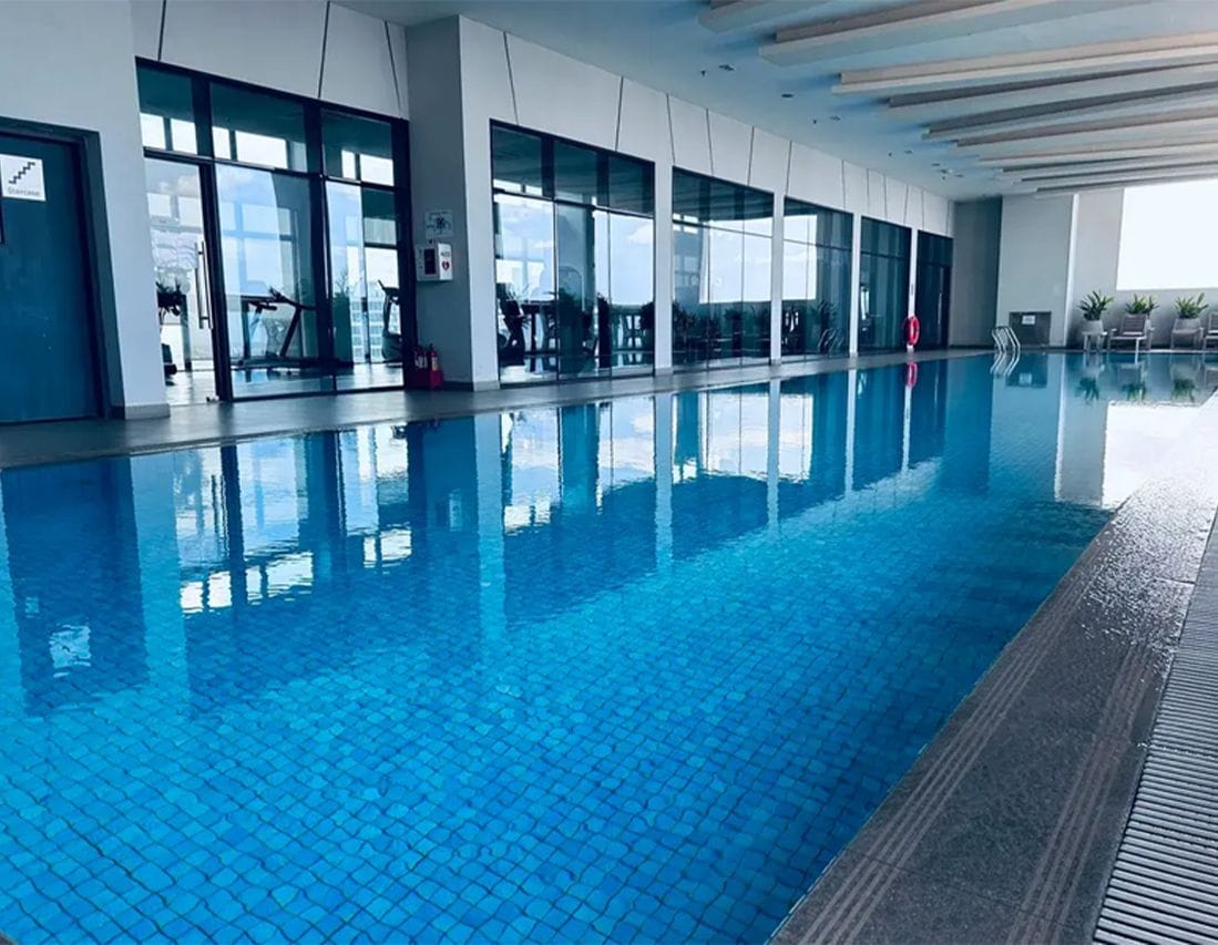An indoor swimming pool with clear glass walls, a tiled floor, and a view of the sky.