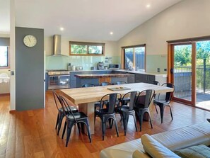 Een moderne keuken met een centraal eiland, een eethoek met stoelen en een grote schuifpui naar een buitenruimte.