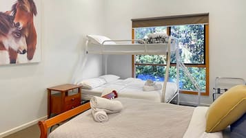 Een slaapkamer met een stapelbed, nachtkastje, raam met uitzicht op groen en een schilderij van paarden.