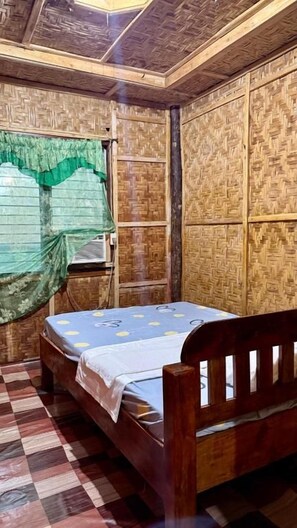 A room with a bed, a window with a green curtain, and a wall with a woven pattern. - Felban's Farm (Carmen, Bohol)