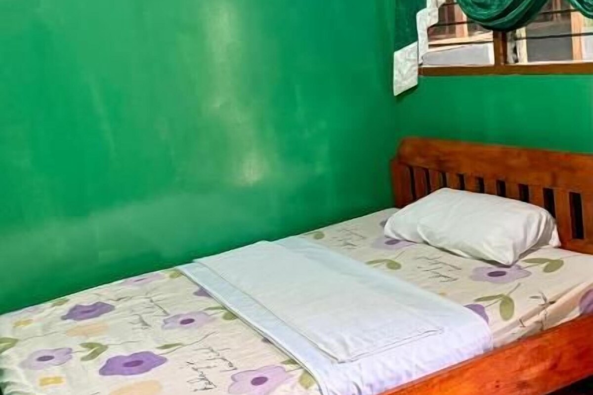 A single bed with a floral bedspread, a wooden headboard, and a green wall.