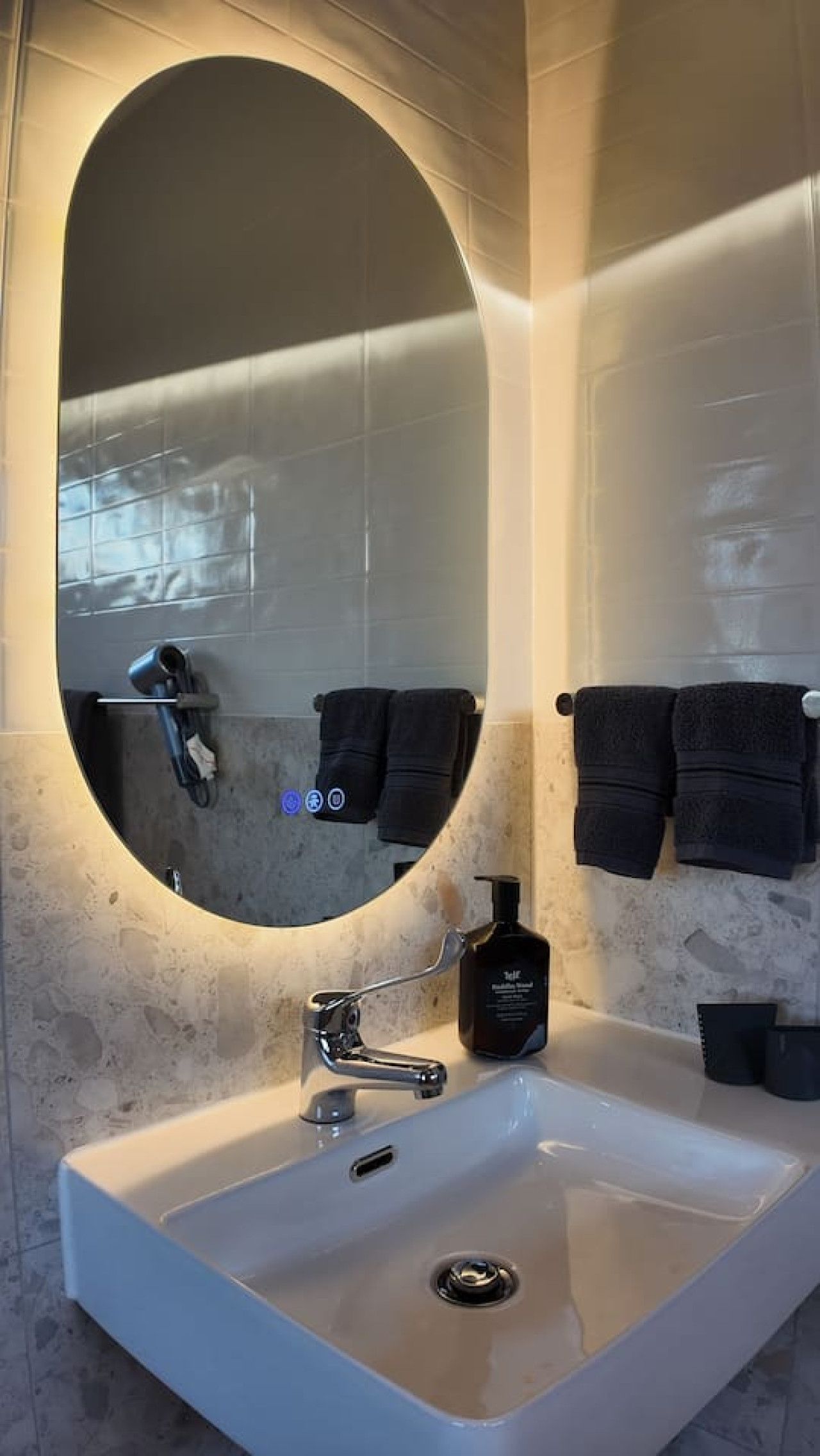Un bagno con uno specchio ovale grande, un lavandino bianco e due asciugamani neri su ganci.
