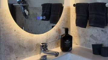 Un bagno con uno specchio ovale grande, un lavandino bianco e due asciugamani neri su ganci.