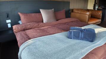 Un letto rifatto con una coperta e dei cuscini blu, un divano in pelle marrone e una testiera con un interruttore della luce.