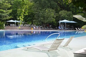 A swimming pool with lounge chairs and umbrellas, surrounded by trees. - Alessi's Studio • Coastal Chapter Mactan (Lapu-Lapu)