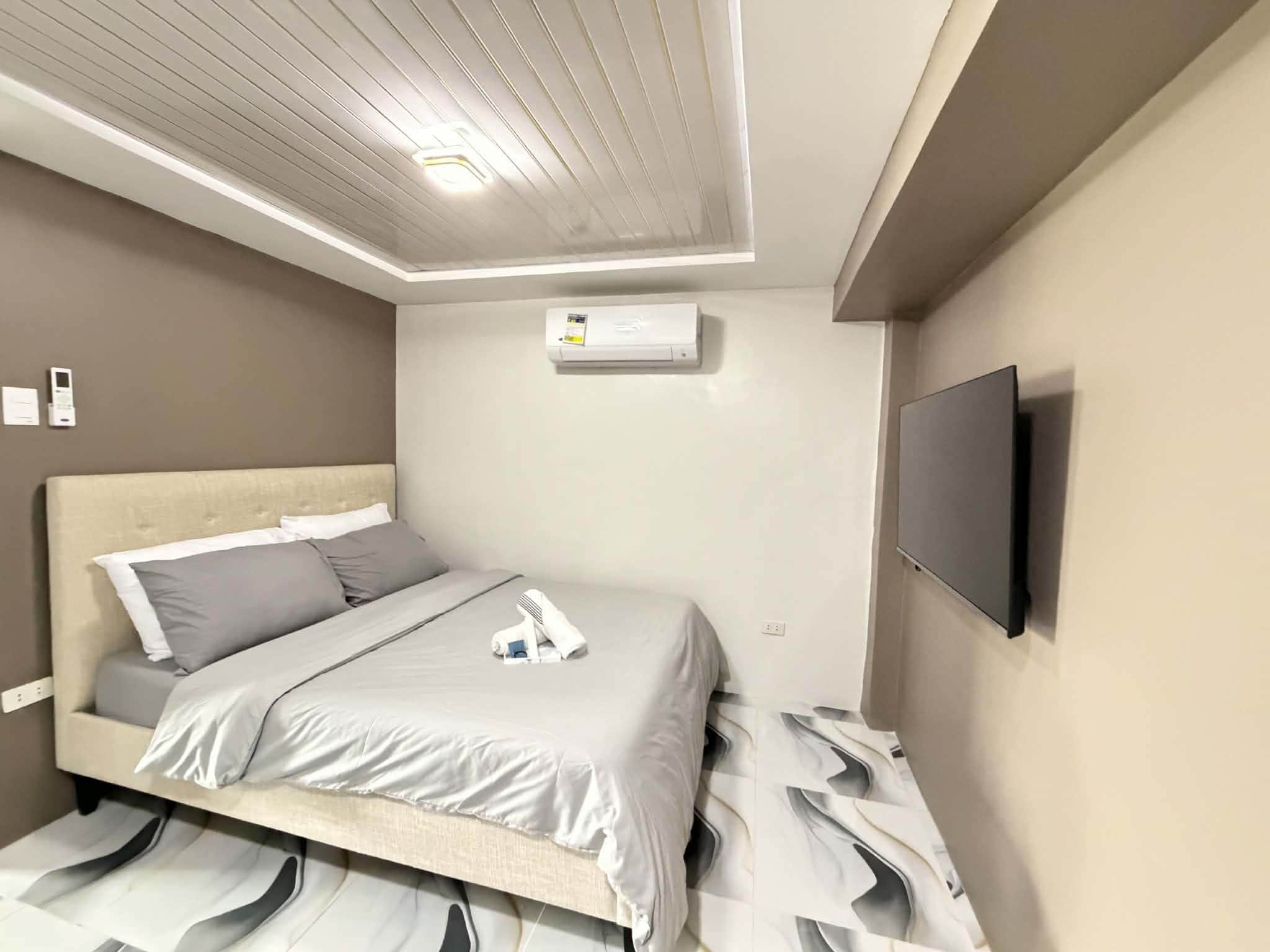 Una habitación de hotel con una cama, un televisor de pantalla plana montado en la pared y un equipo de aire acondicionado en el techo.