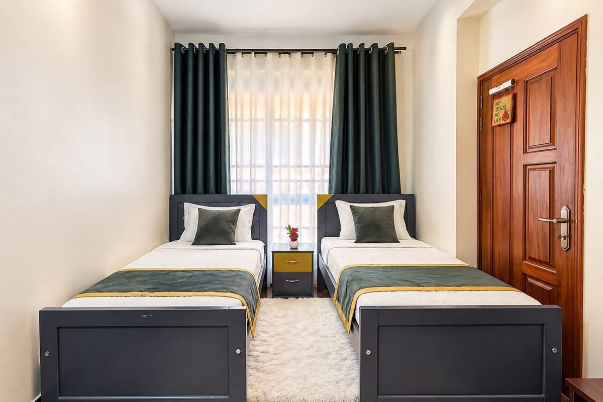 A hotel room with two beds, a wooden door, and a nightstand with a vase.