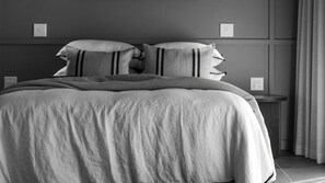Een bed met een gestreept deken en kussens, een nachtkastje en een lichtschakelaar aan de muur.