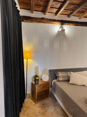 A bedroom with a bed, a nightstand, a lamp, and a potted plant. - Bramante Collection – Fico Apartment By RHR (ROMA)