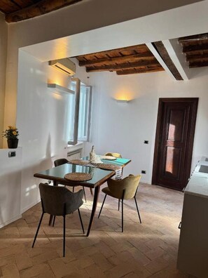 A dining area with a table and chairs, a window, and a door. - Bramante Collection – Fico Apartment By RHR (ROMA)
