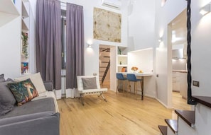 A modern living space with a sofa, a chair, a dining area, and a staircase leading to an upper level. - Bramante Collection – Navona Apartment By RHR (ROMA)
