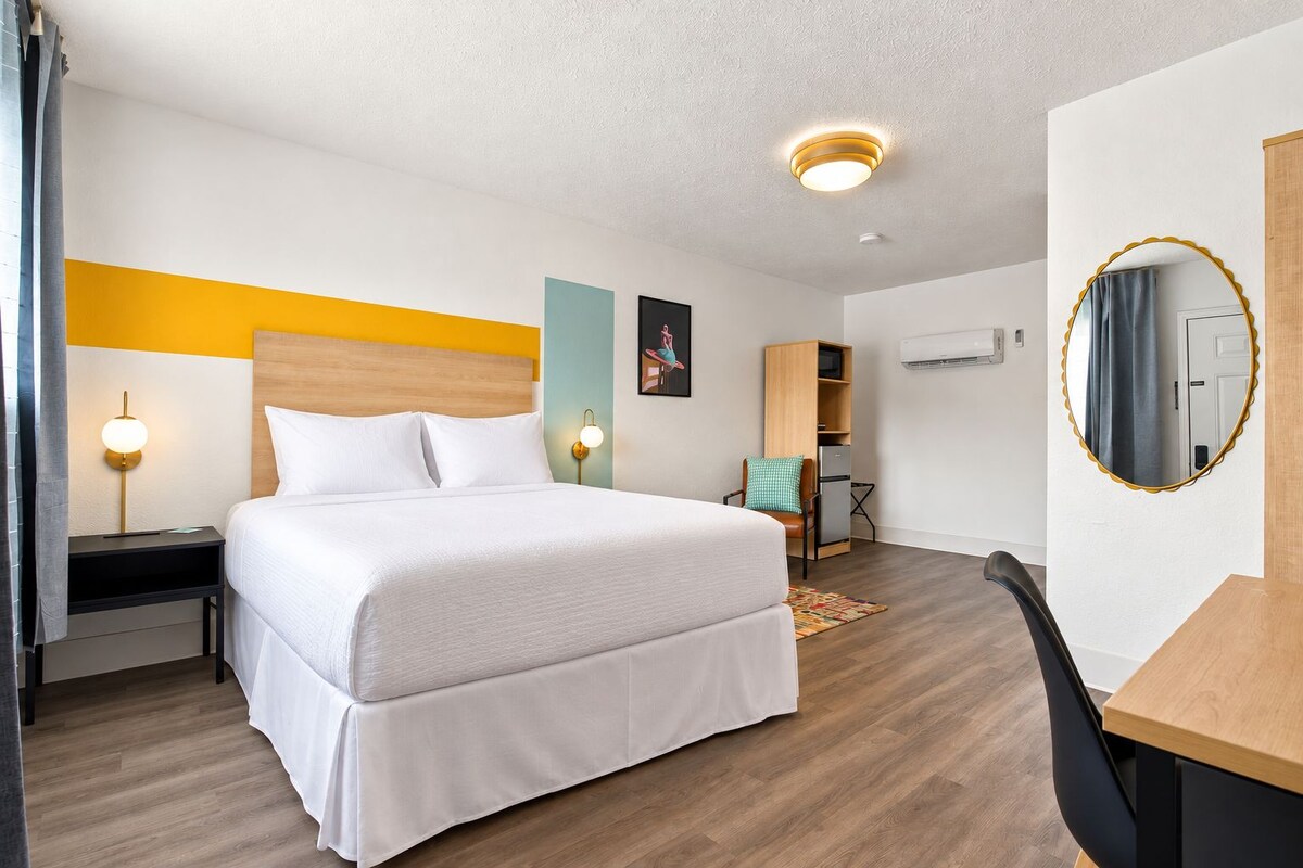 A hotel room with a bed, bedside tables, a desk, a chair, a mirror, and a wardrobe.