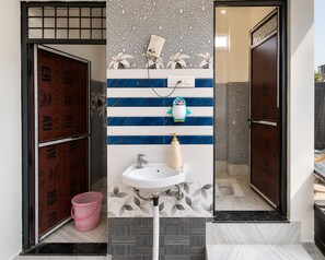 A bathroom with a white sink, a pink bucket, and a decorative penguin ornament. - The Kashi Vibe Homestay (Varanasi)