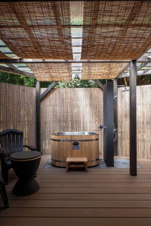 Een hottub met een houten buitenkant, een bankje en een stoel, omgeven door een bamboe hek en een houten terras.