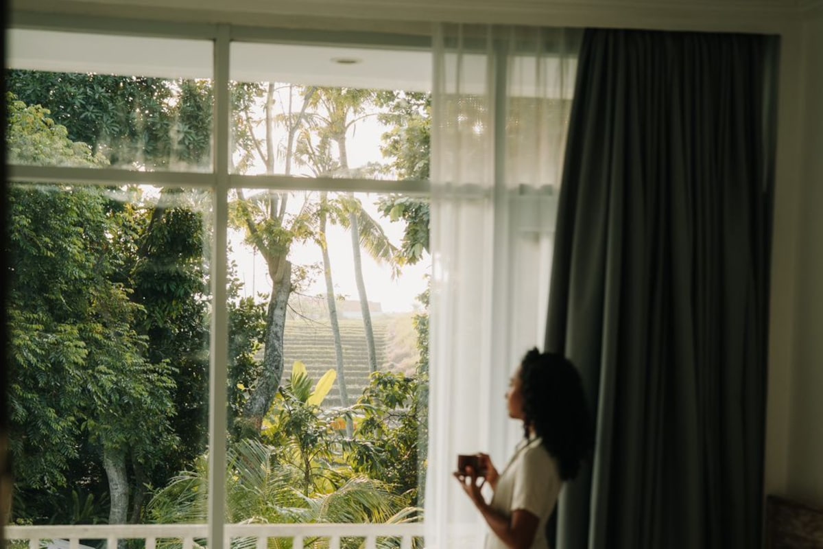 A bedroom with a large window, a bed, a chair, and a table.
