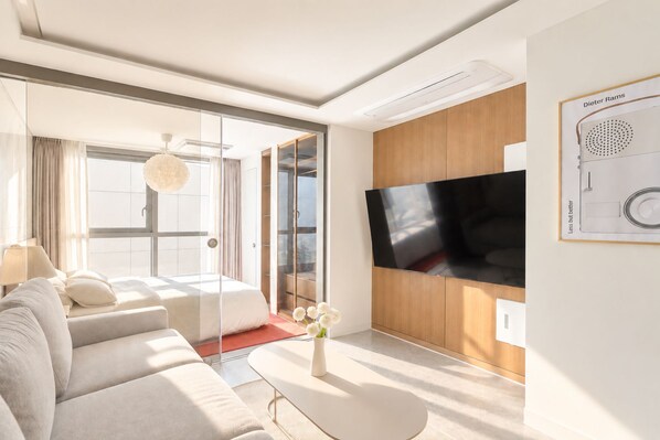 A modern hotel room with a large flat-screen TV, a sofa, a coffee table, and a view through a glass door. - Hotel Comfort, Home Freedom _Studio Double_UH FLAT Seocho New Wing (Seoul)