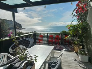 An outdoor seating area with a view of the ocean, a table, chairs, and potted plants. - Shipwreck Bay beach house, surf and sunsets off the deck (Ahipara)