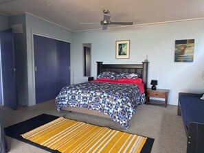 A bedroom with a bed, a nightstand, a ceiling fan, and a door. - Shipwreck Bay beach house, surf and sunsets off the deck (Ahipara)