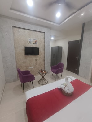 A hotel room with a bed, two purple chairs, a small table, a television, and a wardrobe. - Radha Madhav Homestay (Varanasi)
