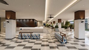 Un hall d’entrée spacieux avec un comptoir de réception, des coins salon et un sol à carreaux.