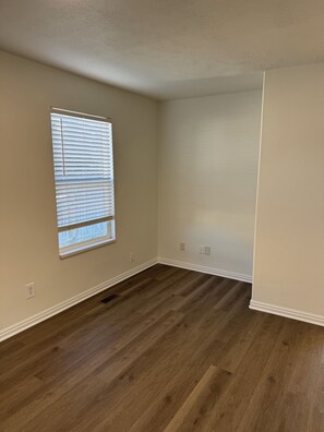 Una habitació amb un gran finestral, terres de parquets i parets blanques.