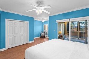 Une chambre dotée d’un grand lit, d’un ventilateur de plafond et offrant une vue sur l’extérieur grâce à une porte-fenêtre coulissante.