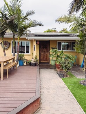 Een huis met een houten terras, plantenpotten en een voordeur.