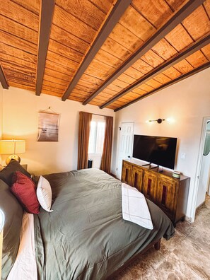 Een slaapkamer met een bed, een televisie, een lamp en een raam met gordijnen.