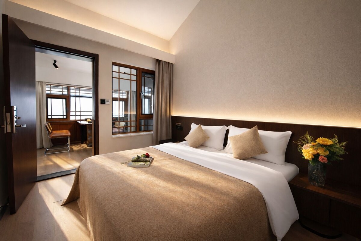 A hotel room with a bed, bedside table, and a view of the outside.