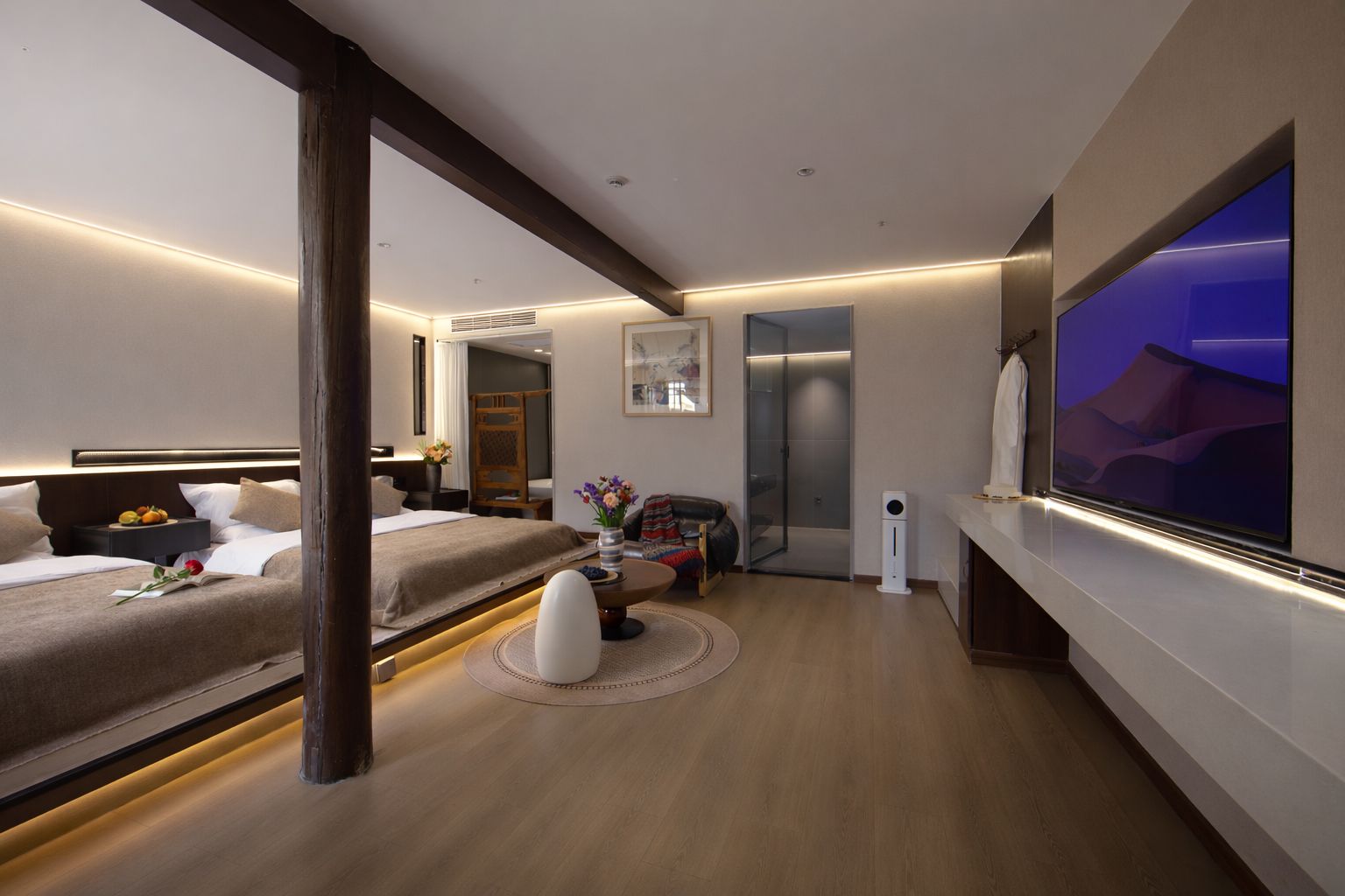 A modern hotel room with a large bed, bedside tables, a flat-screen TV, and a small seating area with a round table.