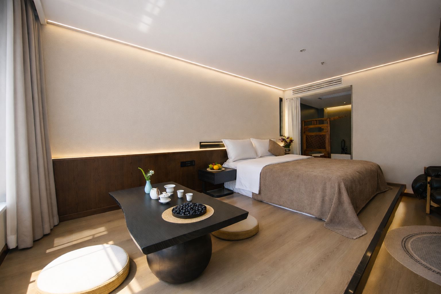 A modern hotel room with a bed, bedside table, and a small seating area.