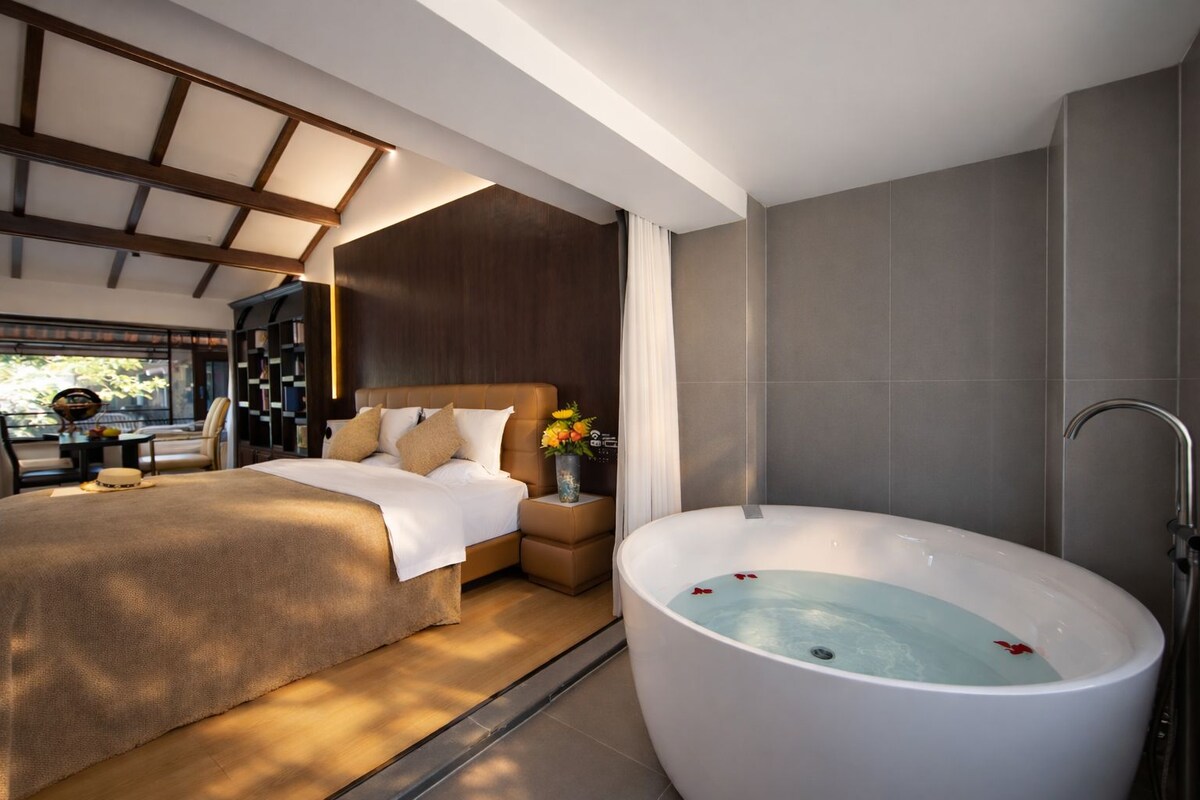 A modern bedroom with a large bed, a sitting area with a table and chairs, and a large bathtub.