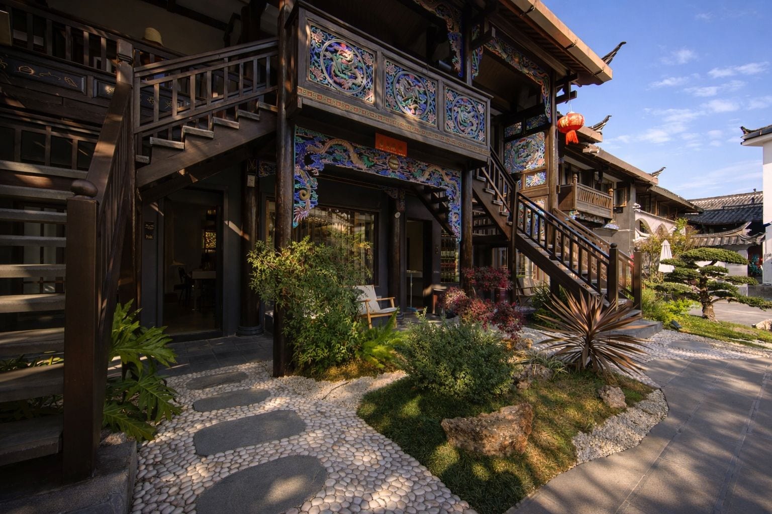 A traditional building with ornate decorations, a staircase, and a garden with rocks and plants.