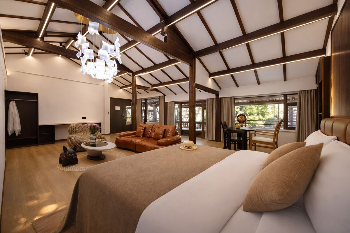 A spacious room with a large bed, a brown leather sofa, a dining table, and a chandelier.