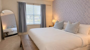 Una camera da letto con un letto, una panca, un comodino con lampade, uno specchio e una finestra con tende.