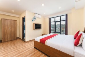 A hotel room with a large bed, a wardrobe, a television, and a window with a city view. - Pashupati Front Hotel (Kathmandu)