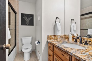 Ein Badezimmer mit Toilette, einem Waschbecken mit Marmorplatte, einem Handtuchhalter und einem gerahmten Bild an der Wand.