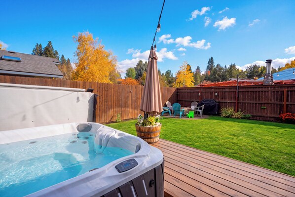 Een achtertuin met een jacuzzi, een houten terras en een omheind gebied met tuinmeubilair.