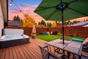Een houten terras met een jacuzzi, buitenmeubilair en een lichtslingering voor een zonsondergang.