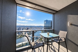 Een balkon met een glazen tafel en stoelen, met uitzicht op een rivier en stadsbeeld.