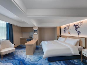 A hotel room with a bed, a desk, a chair, a small kitchenette, and a world map on the wall. - Kyriad Hotel (Shenzhen)