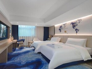 A hotel room with a large bed, a desk, a chair, a world map on the wall, and a blue carpet. - Kyriad Hotel (Shenzhen)